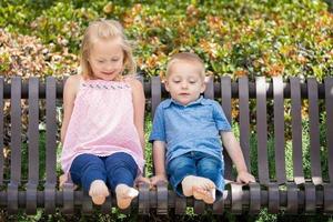 hermana joven y hermano divirtiéndose en el banco en el parque foto