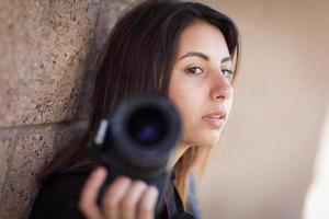 joven fotógrafa étnica adulta contra la pared sosteniendo la cámara. foto