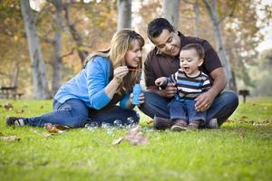 Happy Mixed Race Ethnic Family Playing with Bubbles In Park photo