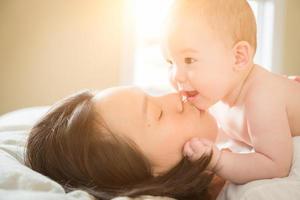 Bebé chino y caucásico de raza mixta acostado en la cama con su madre foto