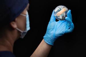 enfermera o médico con mascarilla y guantes quirúrgicos sosteniendo el planeta tierra vendado foto