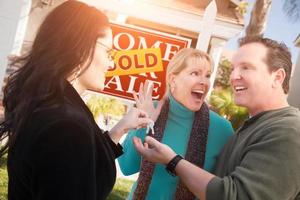 Hispanic Female Real Estate Agent Handing Over New House Keys to Happy Couple In Front of Sold For Sale Real Estate Sign photo