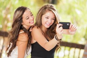 dos atractivas novias de raza mixta usando sus teléfonos celulares inteligentes para selfie al aire libre foto