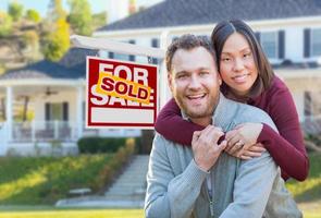 Mixed Race Caucasian and Chinese Couple In Front of Sold For Sale Real Estate Sign and House. photo