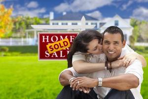 pareja hispana, nuevo hogar y letrero de bienes raíces vendidos foto