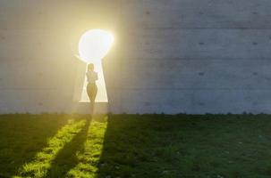 mujer de pie a la luz del sol brillante que brilla a través del ojo de la cerradura en la pared de hormigón en el campo de hierba y rocas. foto