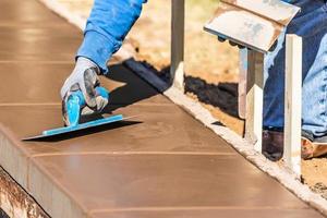 Construction Worker Using Trowel On Wet Cement Forming Coping Around New Pool photo