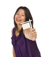 mujer multiétnica sosteniendo un pequeño cartel de bienes raíces en blanco en la mano foto