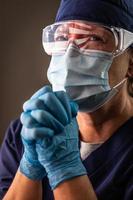 American Flag Reflecting on Distressed Praying Female Medical Worker Wearing Protective Face Mask and Goggles photo