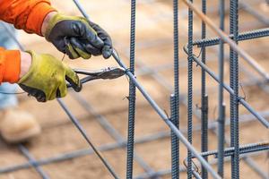 Trabajador que asegura la estructura de barras de refuerzo de acero con la herramienta de corte de alicates de alambre en el sitio de construcción foto