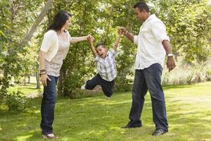 madre hispana y padre balanceando a su hijo en el parque foto