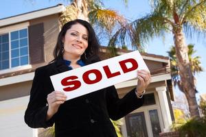 Attractive Hispanic Woman Holding Sold Sign In Front of House photo