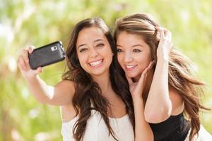 dos atractivas novias de raza mixta usando sus teléfonos celulares inteligentes para selfie al aire libre foto