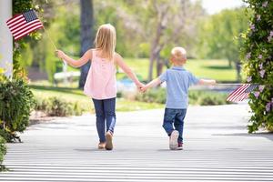 hermana joven y hermano tomados de la mano y ondeando banderas americanas en el parque foto