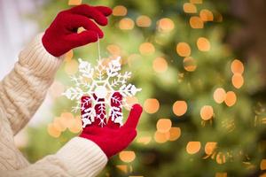 mujer con mitones rojos de temporada sosteniendo adornos navideños de copos de nieve blancos foto