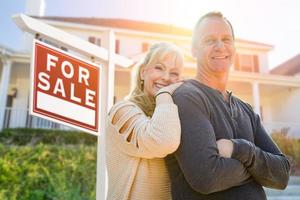 Attractive Middle-aged Couple In Front House and For Sale Real Estate Sign photo