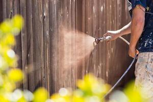 Professional Painter Spraying Yard Fence with Stain photo