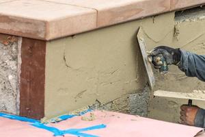 trabajador de baldosas aplicando cemento con paleta en el sitio de construcción de la piscina foto