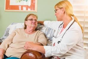 Happy Smiling Doctor or Nurse Talking to Senior Woman in Chair At Home photo