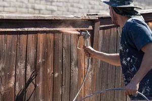 Professional Painter Spraying Yard Fence with Stain photo