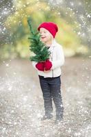 Baby Girl In Mittens Holding Small Christmas Tree with Snow Effect photo