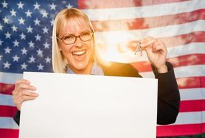 mujer joven sosteniendo las llaves de la casa y un cartel en blanco frente a la bandera estadounidense foto