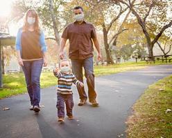 feliz familia étnica de raza mixta caminando en el parque con mascarilla médica foto