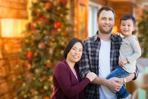Mixed Race Chinese and Caucasian Parents and Child Indoors In Front of Christmas Tree. photo