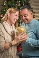 joven, carrera mezclada, pareja, con, presente, cerca, árbol de navidad foto