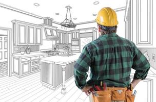 contratista masculino con casco y cinturón de herramientas mirando el dibujo personalizado de la cocina en blanco. foto