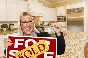 mujer joven con cartel vendido y llaves dentro de la nueva cocina foto