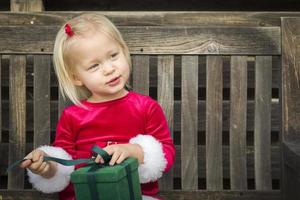 Adorable Little Girl Unwrapping Her Gift on a Bench photo