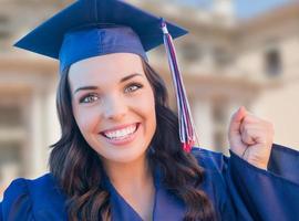 Happy Graduating Mixed Race Woman In Cap and Gown Celebrating on Campus. photo