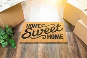 alfombra de bienvenida hogar dulce hogar, cajas de mudanza y plantas en pisos de madera dura foto