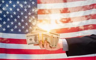 Hand Holding Stacks of Cash In Front of American Flag photo