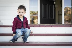 Melancholy Mixed Race Boy Sitting on Front Porch Steps photo