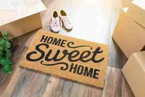 alfombra de bienvenida hogar dulce hogar, cajas de mudanza, zapatos rosas y plantas en pisos de madera dura foto