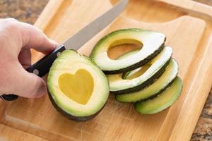 Male Hand Prepares Fresh Cut Avocado With Heart Shaped Pit Area On Wooden Cutting Board photo