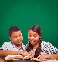 pizarra en blanco detrás de un niño y una niña hispanos divirtiéndose estudiando juntos foto