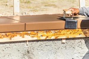 trabajador de la construcción que usa una bordeadora de acero inoxidable en cemento húmedo que forma una nueva piscina foto