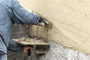 trabajador de baldosas aplicando cemento con paleta en el sitio de construcción de la piscina foto