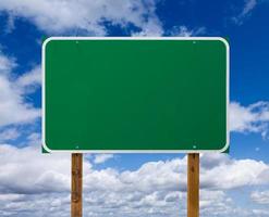 Blank Green Road Sign with Wooden Posts Over Blue Sky and Clouds photo