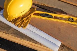 Abstract of Constrcution Hard Hat, Gloves, Level and House Plans Resting on Wood Planks photo