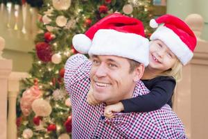 padre e hija con sombreros de santa frente al árbol de navidad decorado. foto