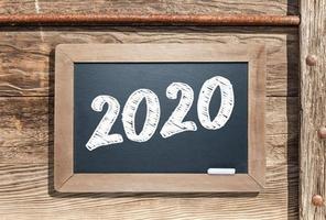 2020 Written on Slate Chalk Board Against Aged Wood and Pipe Background photo