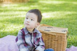 Young Mixed Race Boy Sitting in Park Near Picnic Basket photo