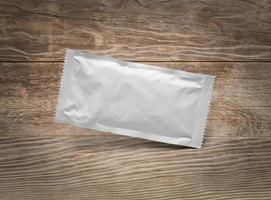 Blank White Condiment Packet Floating on Aged Wood Background photo