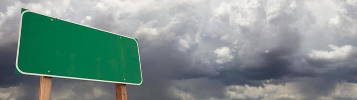 señal de carretera verde en blanco contra la ominosa bandera de fondo del cielo tormentoso nublado foto