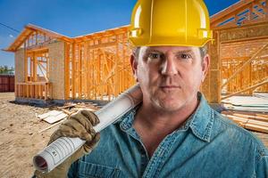 Serious Contractor in Hard Hat Holding Floor Plans At Construction Site. photo