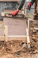 Construction Worker Leveling Wet Cement Into Wood Framing photo